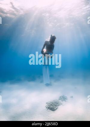 Femme freediver en bikini posant sous l'eau sur fond de mer sablonneux avec des ailerons. Femme attrayante dans l'océan bleu Banque D'Images