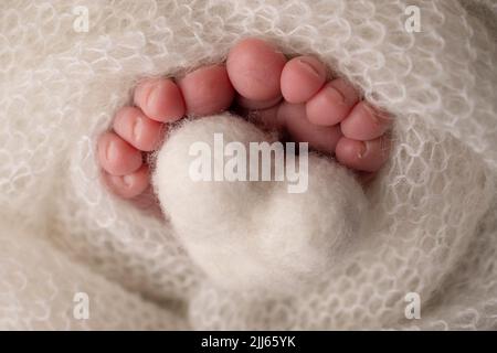 Coeur blanc tricoté dans les jambes d'un bébé. Pieds doux d'un nouveau-né dans une couverture de laine blanche. Banque D'Images