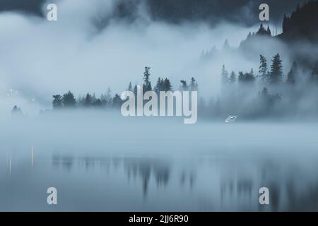 Moody, brouillard atmosphérique en soirée au-dessus du lac Kootenay à Nelson, C.-B., Canada, avec une cabine isolée et isolée le long du bord de mer. Banque D'Images