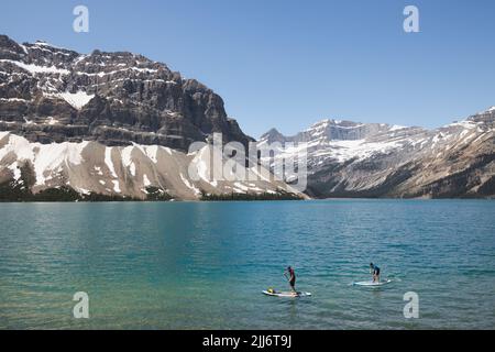 Lac Bow, Canada - 1 juillet 2022 : deux hommes profitent de loisirs de plein air en été sur des planches à aubes de stand-up sur l'eau bleue du lac Bow dans le parc national Banff Banque D'Images