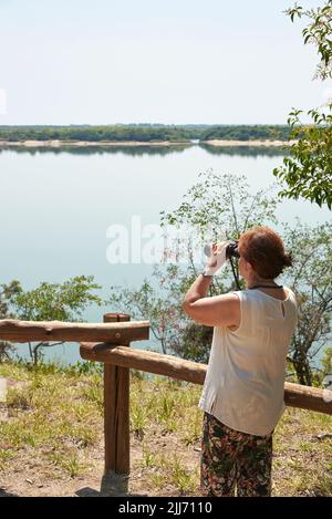 Femme hispanique mature regardant à travers des jumelles depuis un point de vue dans le parc national d'El Palmar, entre Rios, Argentine. Concepts : vie active, voyage Banque D'Images