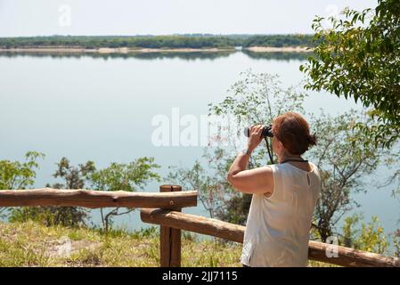 Femme hispanique mature regardant à travers des jumelles depuis un point de vue dans le parc national d'El Palmar, entre Rios, Argentine. Concepts : vie active, voyage Banque D'Images