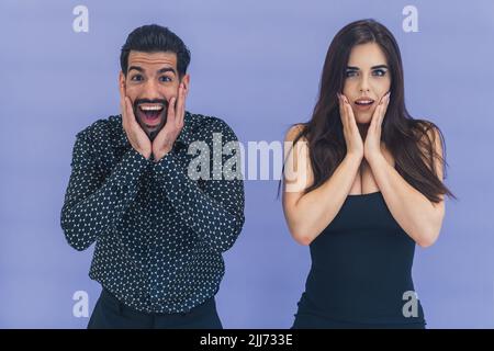 Choc, étonnement. Des expressions faciales surprises de couple hétérosexuel interracial debout devant la caméra en studio, regardant la caméra, touchant leurs visages. Fond violet. Photo de haute qualité Banque D'Images