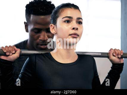 Les meilleurs entraîneurs ont votre dos. Un jeune homme et une jeune femme s'entraîner avec un barbell dans une salle de gym. Banque D'Images