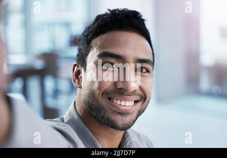 Réglage de ma webcam. Un beau jeune agent de service à la clientèle assis seul dans le bureau et prenant un selfie. Banque D'Images