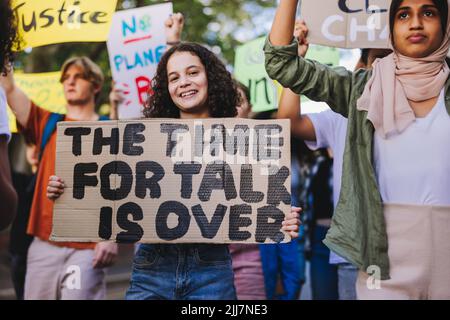 Une jeune fille heureuse tenant une affiche lors d'une manifestation contre le changement climatique. Un groupe de jeunes militants manifestent contre le réchauffement climatique. Jeune peopl multiculturel Banque D'Images