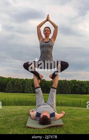 Un jeune couple fait de l'acro yoga dans le parc. Homme allongé sur l'herbe et femme d'équilibrage dans ses pieds Banque D'Images