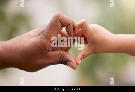 Les gens les plus petits prennent la plus grande pièce de votre coeur. Un homme et son enfant méconnaissables faisant un geste en forme de coeur avec leurs mains dans un Banque D'Images