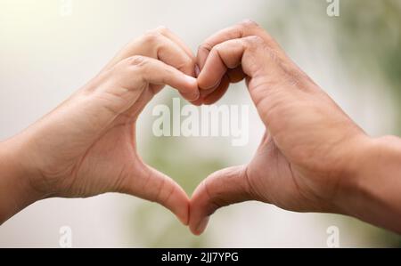 L'amour nous permettra de rester connectés. Un homme et une femme méconnaissables faisant un geste en forme de cœur avec leurs mains dans un jardin. Banque D'Images