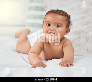 Ce n'est pas seulement le soleil qui illumine une pièce. Un adorable bébé garçon jouant sur le lit à la maison. Banque D'Images