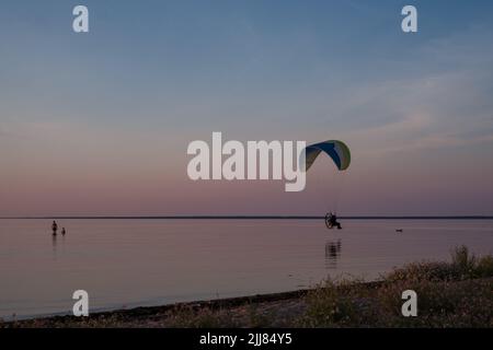 Le pilote de parapente vole dans le ciel pendant le coucher du soleil sur la belle plage. Silhouette de paraplane. Concept de vacances et de voyages d'aventure. Banque D'Images