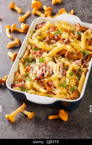 Gratin préparé à partir de pâtes de penne avec chanterelle champignons, viande et fromage en gros plan dans un plat de cuisson en céramique sur la table. Vertical Banque D'Images