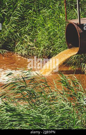 Déchets industriels sous forme d'eau orange s'écoulant de la pipe dans la rivière Banque D'Images