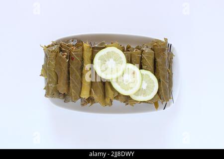 Cuisine turque ou grecque nourriture Yaprak Sarma (enveloppé farci) avec des tranches de citron. Feuilles de raisin farcies au riz isolées sur fond blanc. Banque D'Images