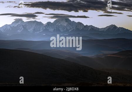 Nuages sombres sur des montagnes enneigées au coucher du soleil entouré de champs Banque D'Images