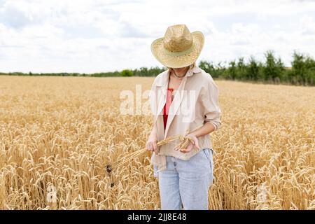 Une femme en chapeau debout sur un champ de blé d'or. Elle tient un bouquet d'épillets dans ses mains. Banque D'Images