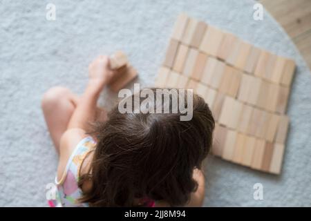 Enfant caucasien fille, 5 ans, jouant avec des blocs de bois sur le plancher, assis sur la moquette beige intérieur. Banque D'Images