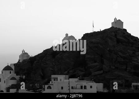 Les touristes explorant les petites chapelles pittoresques en haut de la colline sur l'île magnifique d'iOS Grèce tandis que le soleil se couche en noir et blanc Banque D'Images