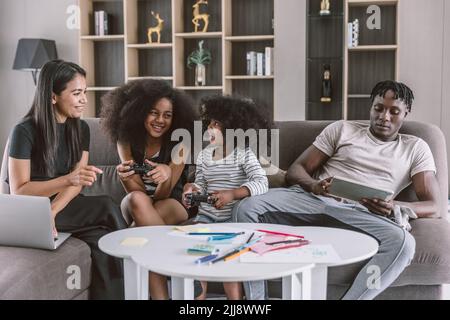 Détendez-vous dans une famille multiraciale joyeuse, parents avec deux enfants assis sur un canapé salon jouant à des jeux vidéo vacances de loisirs ensemble. Banque D'Images