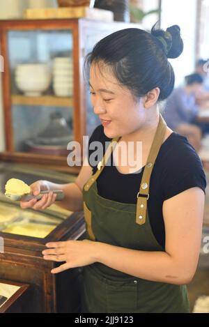 Serveuse vietnamienne montrant une cuillère de glace à la mangue maison dans le café Banque D'Images