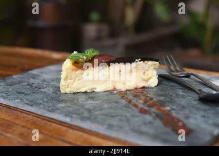 Cheesecake brûlé sur une plaque de pierre avec une feuille de menthe qui bascule sur fond gris de pierre Banque D'Images