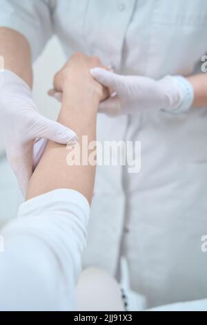 Médecin en gants blancs examinant la main d'un patient Banque D'Images
