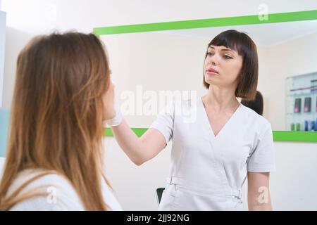 Médecin examinant la peau du visage féminin en centre de cosmétologie Banque D'Images