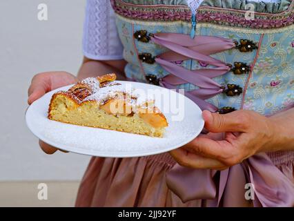 Une femme dans une belle robe traditionnelle de dirndl tenant un morceau de tarte aux pommes maison délicieuse à la fête bavaroise d'octobre (Oktoberfest) (Bavière, Banque D'Images