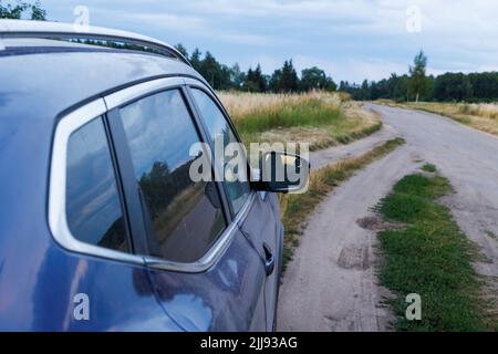 voiture violette sur la route sèche en terre le soir d'été avec de l'herbe jaune haute sèche et une forêt vert foncé sur fond flou Banque D'Images