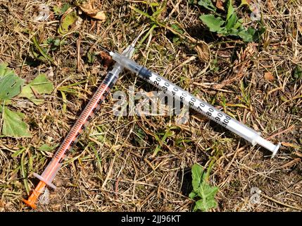 deux seringues infectées abandonnées utilisées par les toxicomanes pour injecter des drogues laissées sur le terrain dans le parc public après utilisation Banque D'Images