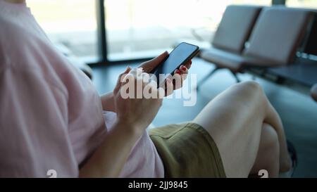 Une femme voyageur avec un smartphone entre ses mains est assise dans la zone de départ de l'aéroport ou de la gare Banque D'Images