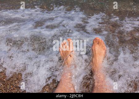 Vue rapprochée des jambes mâles sur la mer pendant la vague en mouvement. Concept de vacances d'été. Banque D'Images