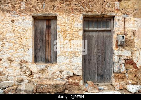 Ancienne façade de maison rurale traditionnelle. Extérieur de cottage en grès patiné avec fenêtre et porte en bois brun fermée. Grèce, vintage abandonné Banque D'Images