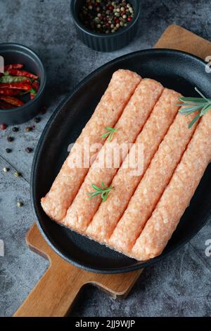 Saucisses maison crues poulet, dinde dans une casserole sur fond sombre avec des épices Banque D'Images