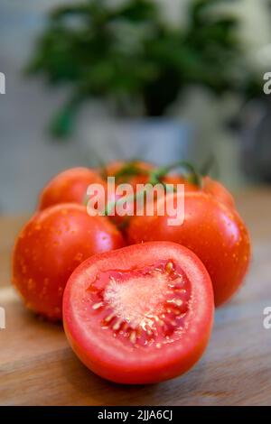 Tomates rouges sur vigne dans la cuisine - tomates fraîches tranchées et entières sur planche à découper en bois - bouquet mûr Solanum lycopersicum et grappe Banque D'Images