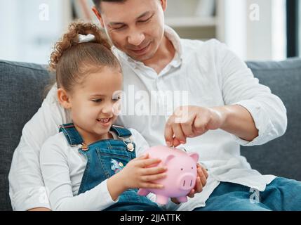 Lui enseigner la valeur de l'argent. Un père enseignant à sa fille d'épargner dans une porcgybank. Banque D'Images