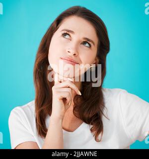 Je me demande... Photo en studio d'une jeune femme attrayante, sur fond bleu. Banque D'Images