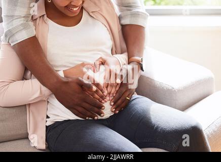 Tellement d'amour déjà. Un couple affectueux et méconnaissable de parents à être assis sur le canapé à la maison. Banque D'Images