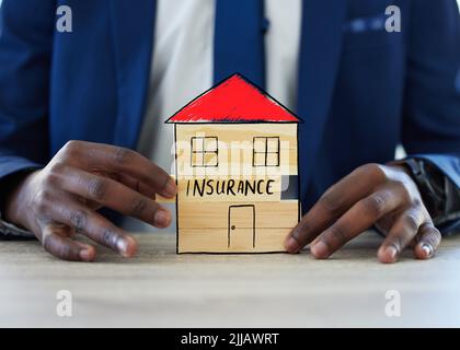 Protégez votre maison pour la tranquillité d'esprit. Un homme d'affaires méconnaissable assemble un bâtiment avec le mot assurance dessus. Banque D'Images