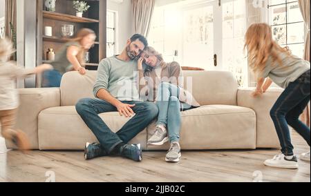 Nous aurons jamais une pause. Deux parents épuisés sur le canapé pendant que les enfants jouent à la maison. Banque D'Images