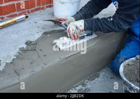 un travailleur utilise une spatule pour distribuer le mélange de ciment le long de la rampe Banque D'Images