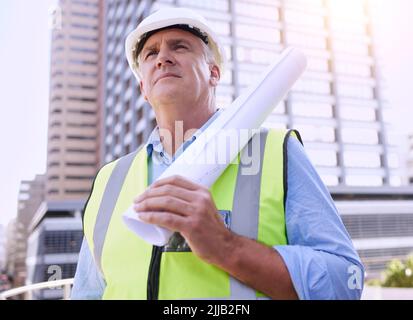 HES prêt à construire quelque chose de grand. Un beau ouvrier de construction mature mâle transportant des plans tout en se tenant à l'extérieur. Banque D'Images