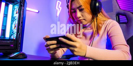 Perdre. Joueur en jouant à des jeux vidéo en ligne avec un smartphone avec des lumières néon, elle échoue au jeu, femme asiatique confuse portant des écouteurs de jeu jouer à la mo Banque D'Images