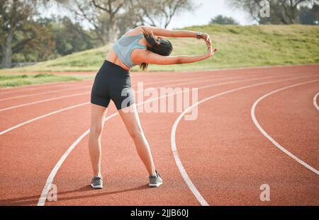 L'étirement est un signal puissant pour renforcer les muscles. Prise de vue arrière d'une jeune athlète qui étire son corps sur une piste de course à pied. Banque D'Images