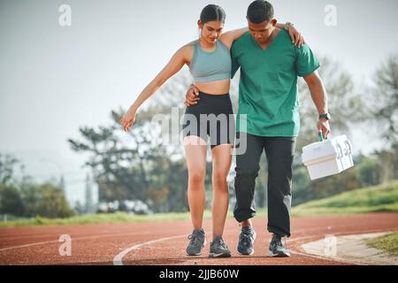 Essayez de ne pas trop exercer de pression sur la blessure. Un paramédic sportif fournissant les premiers soins à un athlète sur une piste de course. Banque D'Images