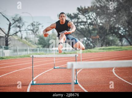 Aucun obstacle trop grand. Tir en longueur d'un jeune athlète de sexe masculin pratiquant des haies sur une piste en plein air. Banque D'Images