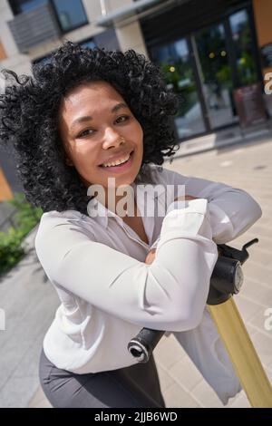 Femme multiraciale en chemise blanche debout sur un scooter Banque D'Images