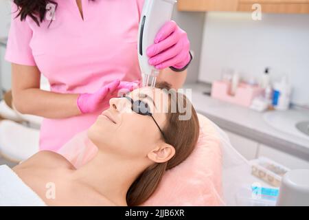 Femme couché avec des lunettes de protection lors d'une procédure de rajeunissement professionnelle Banque D'Images