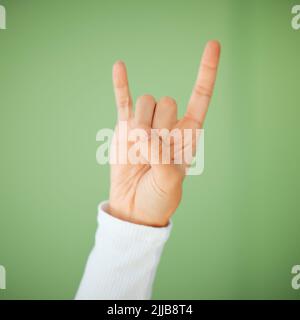 Rock n roll est là pour rester. Une femme méconnaissable montrant un geste rock n roll sur fond vert. Banque D'Images