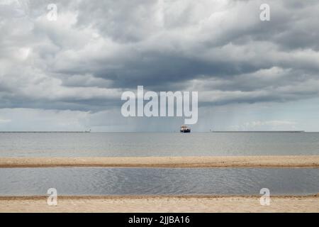 Plage sur la mer Baltique. Navire de transport maritime de fret à l'horizon au-dessus de l'eau. Nuages orageux au-dessus de la mer Banque D'Images